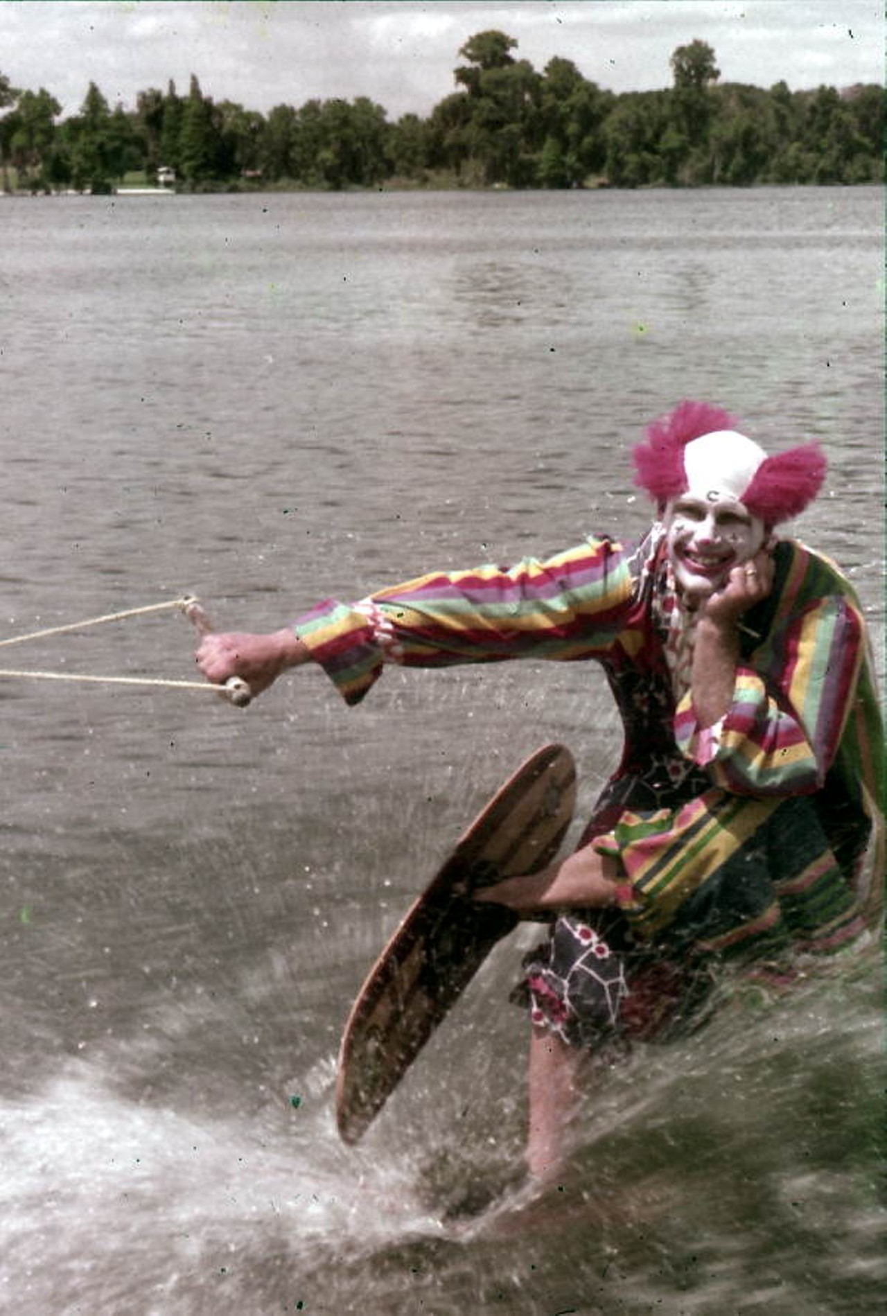 A clown waterskiing and leering.