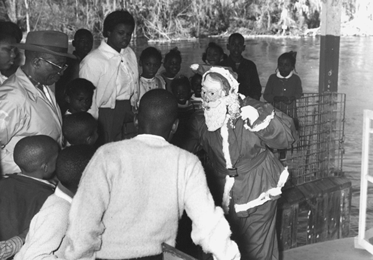 Timothy Howard, dressed as Santa Claus, arrived at Paradise Park on a glass bottom boat. Here he passes out Christmas gifts to the children. Eddie Vereen, wearing a hat, looks on. Photo by Bruce Mozert. By permission of Bruce Mozert. Courtesy of Marion County Black Archives. Reprinted with permission of the University Press of Florida.