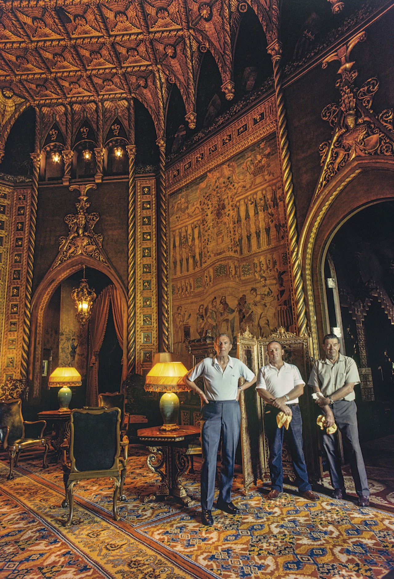 Caretakers in the opulent Hispano-Moresque style drawing room of Marjorie Merriweather Post in her residence at Mar-a-Lago, the fabulous winter villa in Palm Beach, Florida. Three members of her maintenance staff stand in the room, including Mr. Frank Moffat (standing left), responsible for household management as head steward or majordomo (on right). Mrs. Post died in 1973 and before it was sold to Donald Trump to create the Mar-a-Lago Club. The drawing room features antique furniture and tapestries and guilding on architectural features.
