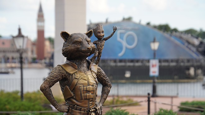 Rocket and Groot Fab 50 statue at Epcot with the 50th-anniversary logo seen on a Harmonious barge LED screen behind them.