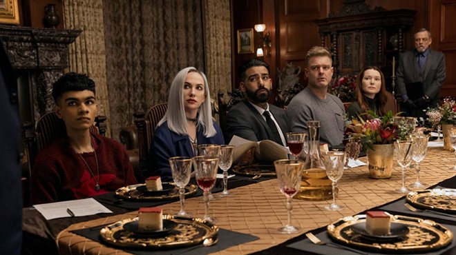 Six people of assorted ages, genders and ethnicities sit at a long, fancy dinner table.