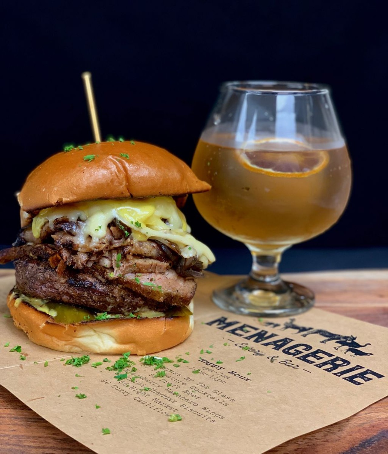 Menagerie Eatery & Bar:Bumble Bee Burger - 8oz. angus, white cheddar, yellow sriracha aioli, caramelized onions, house brisket & pickled English cucumbers on toasted brioche.