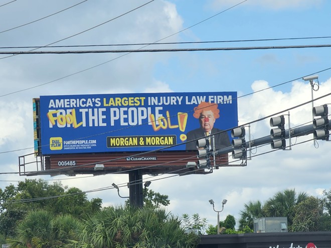 A Morgan & Morgan billboard appears spray-painted over to depict founder John Morgan as a clown. Spotted in Orlando in Sept. 2023. - Corey Thomas