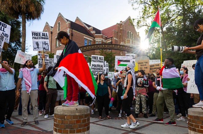 Una niña envuelta en una bandera palestina se encuentra en un poste mientras los manifestantes que apoyan el fin del asedio de Gaza se reúnen en la esquina de University Avenue y 13th Street en la Universidad de Florida en Gainesville el 25 de octubre de 2023.  - La foto de Gabriel.  Velásquez Neira/Fresh Take Florida