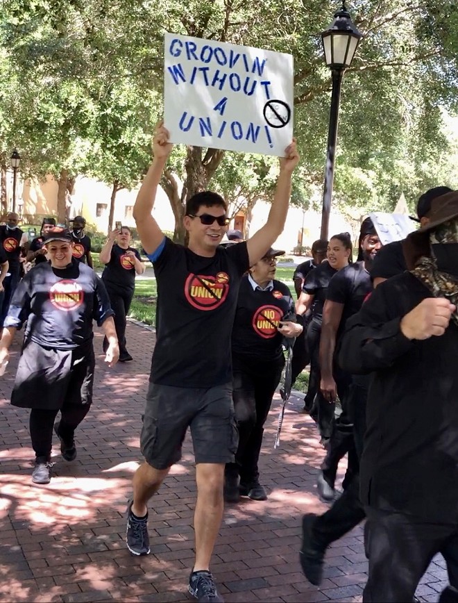 Dining workers march around campus during awkward-vibes 'No Union' rally with one employee of two months holding a sign that reads, "GROOVIN WITHOUT A UNION." April 2023. - McKenna Schueler